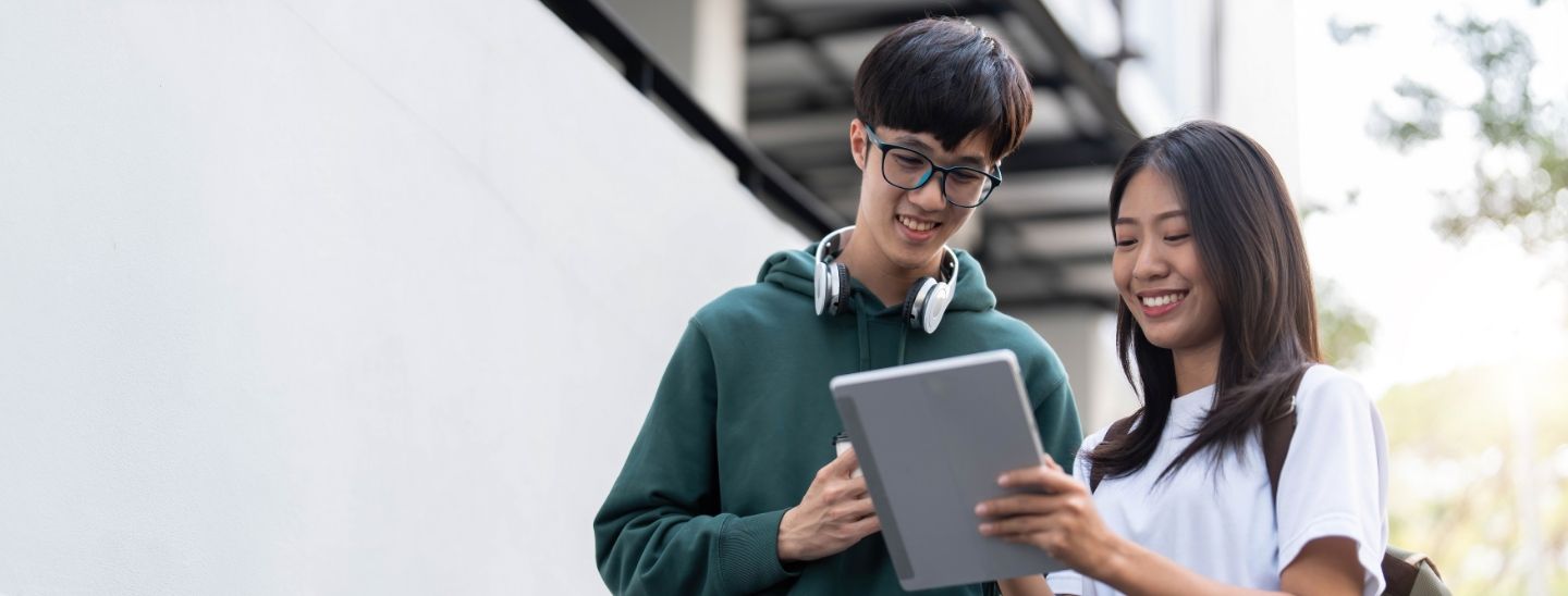Students standing outside, looking at a digital tablet together.