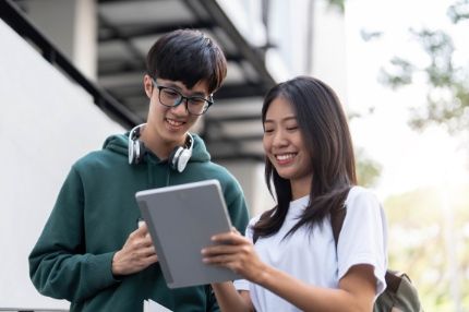 Students standing outside, looking at a digital tablet together.