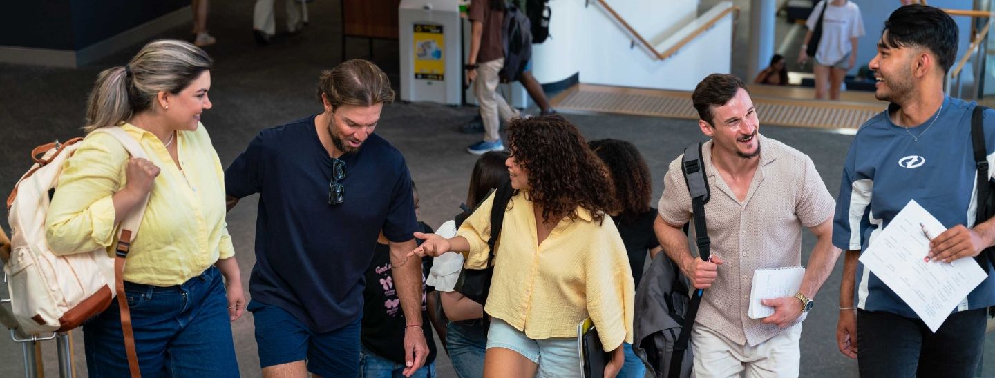 A group of university students walking and talking together in a bright campus hallway.