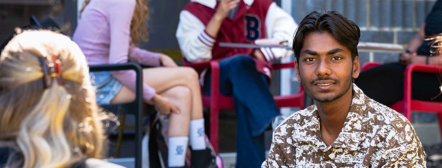 Male student smiling at the camera during a Foundation Program session, seated outdoors with classmates.