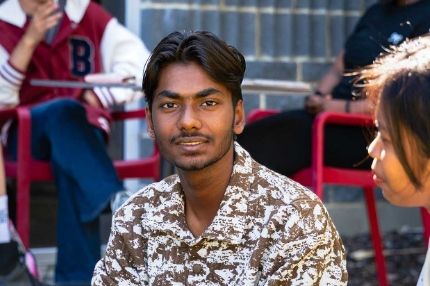Male student smiling at the camera during a Foundation Program session, seated outdoors with classmates