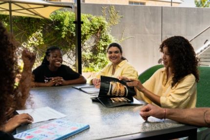 A group of ECC students sitting at a large outdoor table, smiling and discussing a health science textbook