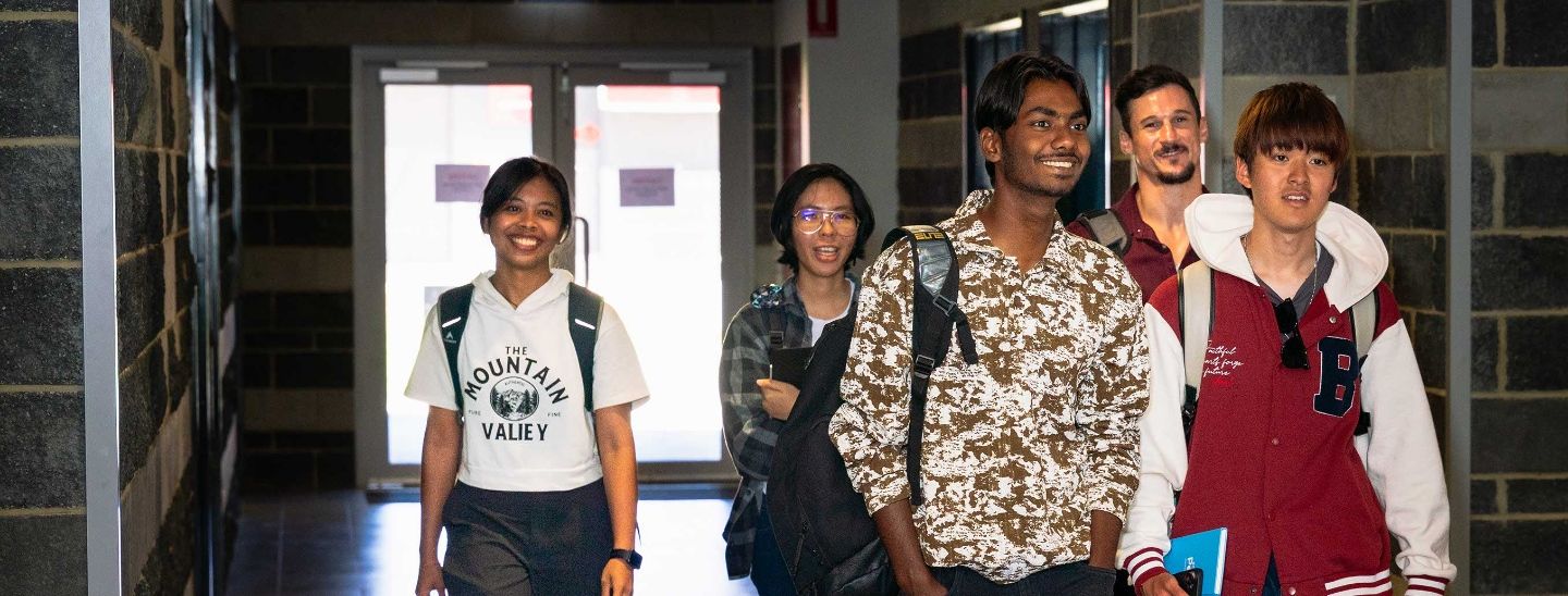 ECC international students carrying backpacks and books while walking through a campus building entrance.