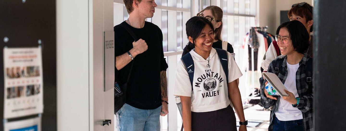 A group of international students under 18 smiling and talking while walking through college campus.
