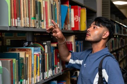 Student selecting a book from a library shelf.