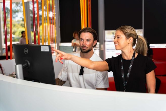 A female in a black t-shirt provides technical guidance to a colleague.