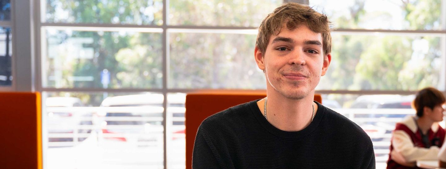 Student sitting at a table writing in a notebook and looking up