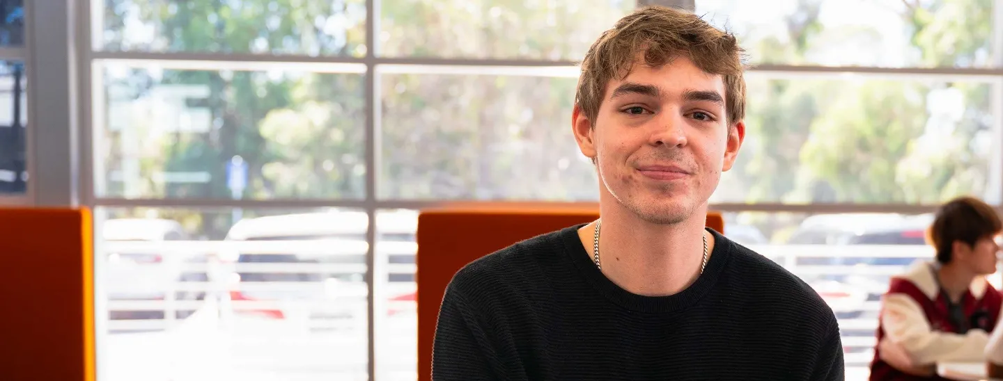 Student sitting at a table writing in a notebook and looking up