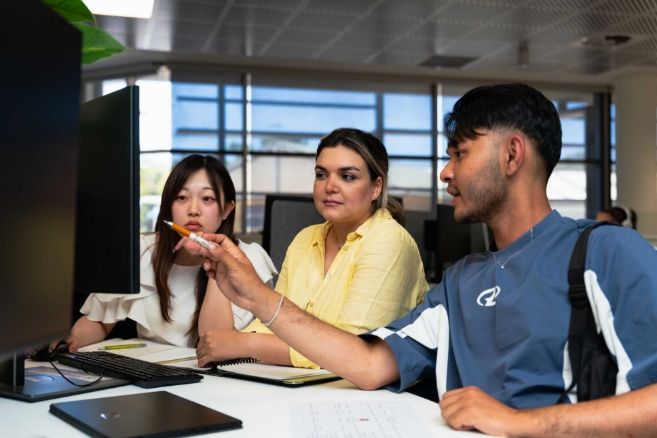 Students discussing academic entry requirements and course materials in a modern campus computer lab.