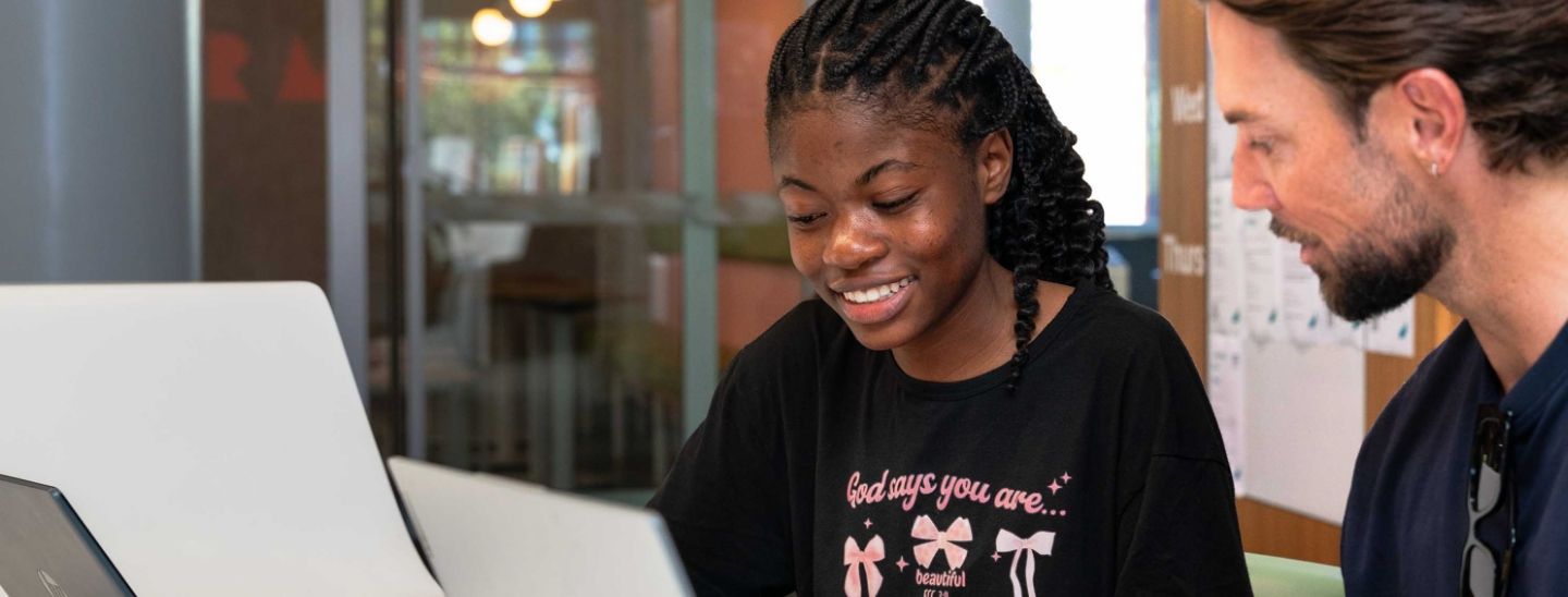 Female student looking at a laptop during a collaboration session with a mentor in a modern office or educational setting.