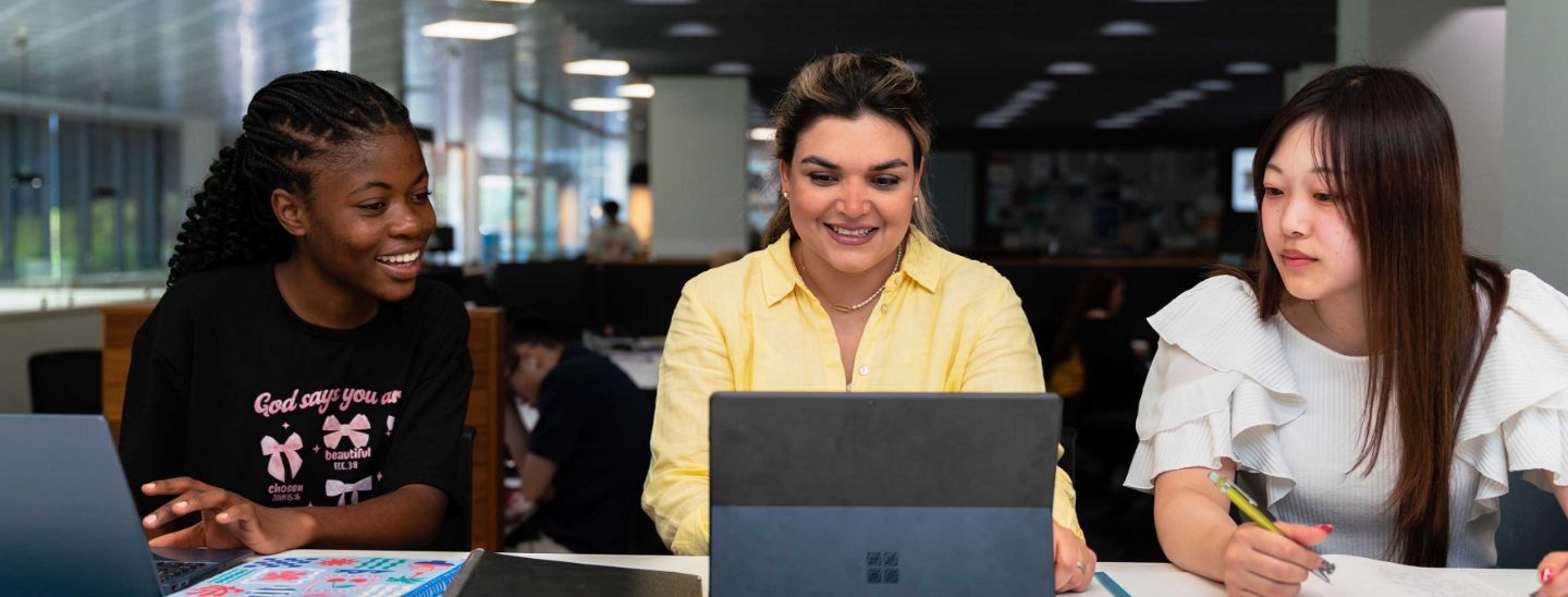 ECC female students smiling and working together on a laptop in a modern library.