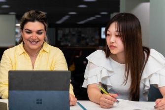 ECC female students smiling and working together on a laptop in a modern library.