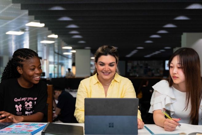 ECC female students smiling and working together on a laptop in a modern library.