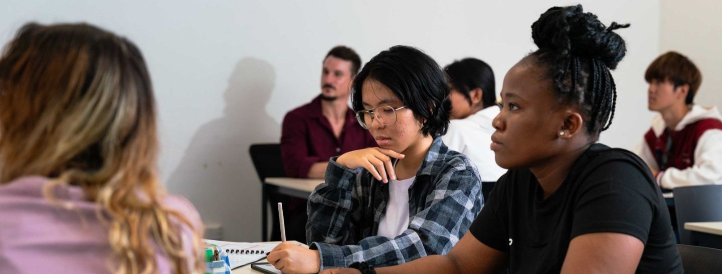 Students discussing English entry requirements and course materials in a modern campus computer lab.
