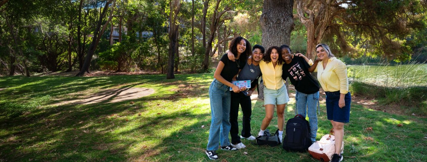 ECC students standing together under a large tree in a sunlit park or campus setting.