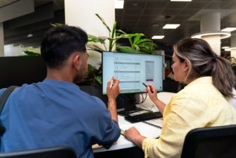 Two students are looking at a computer screen and discussing data displayed on a monitor.