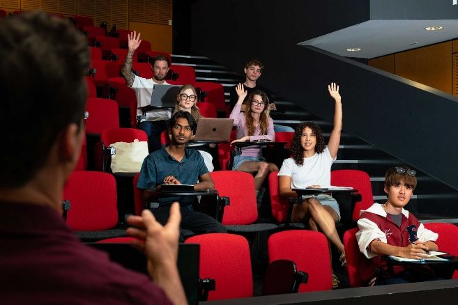 ECC students sitting in red theater-style seats in a lecture hall, some using laptops and smiling toward the camera.