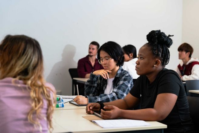 ECC students sitting at desks in a classroom, looking forward and taking notes during a lecture.