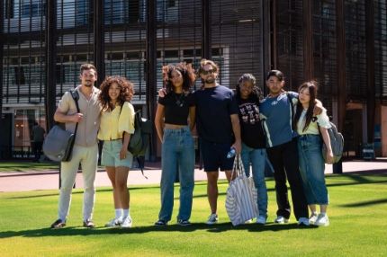 Group of college ECU students with backpacks posing together outside a university building on a bright day.