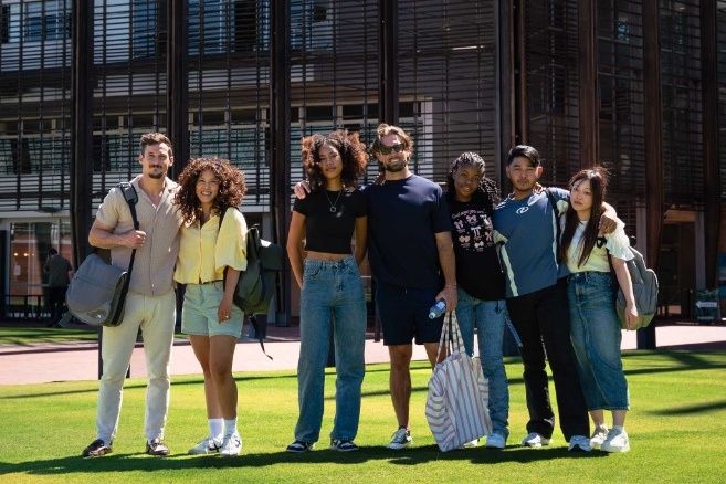 Group of college ECU students with backpacks posing together outside a university building on a bright day.