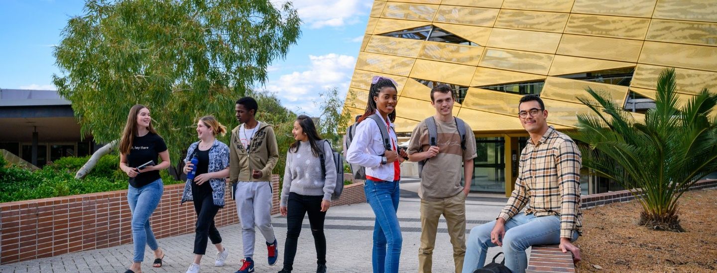 A group of students walking and socialising outside the gold-faceted building at Edith Cowan College.