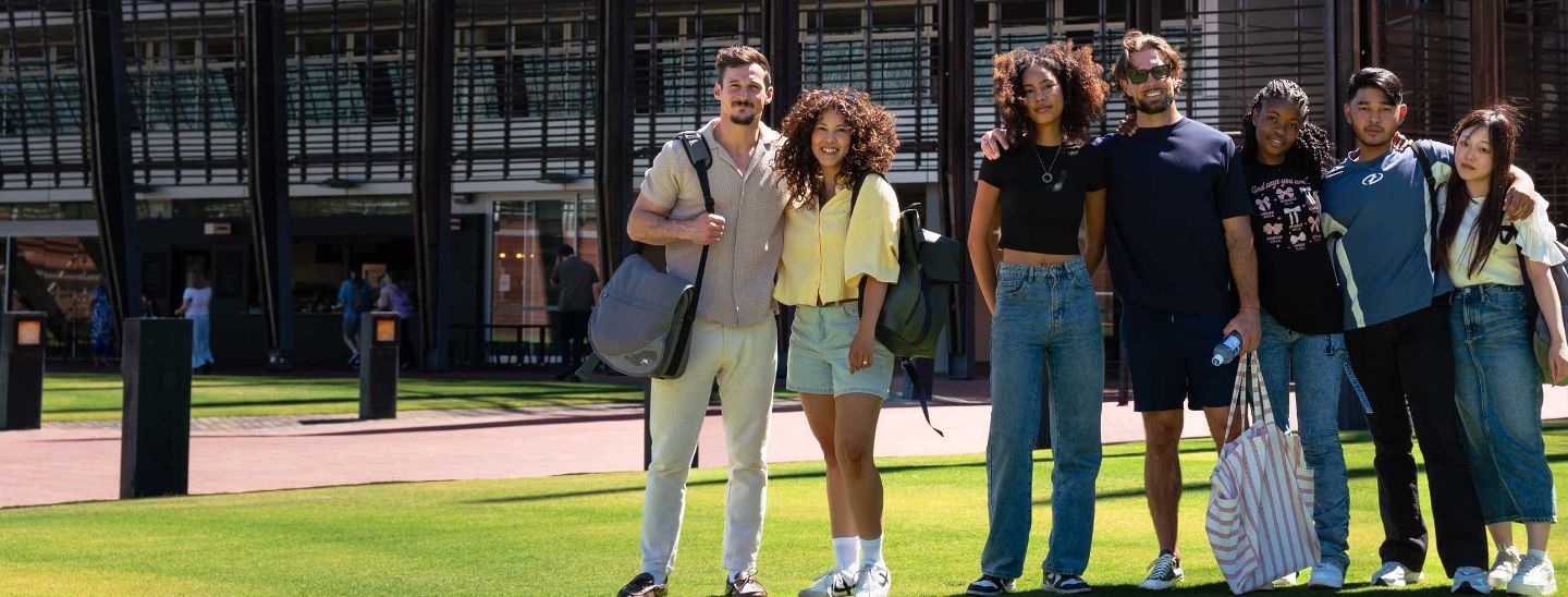 Group of students standing together on a grassy campus, with university building in the background.
