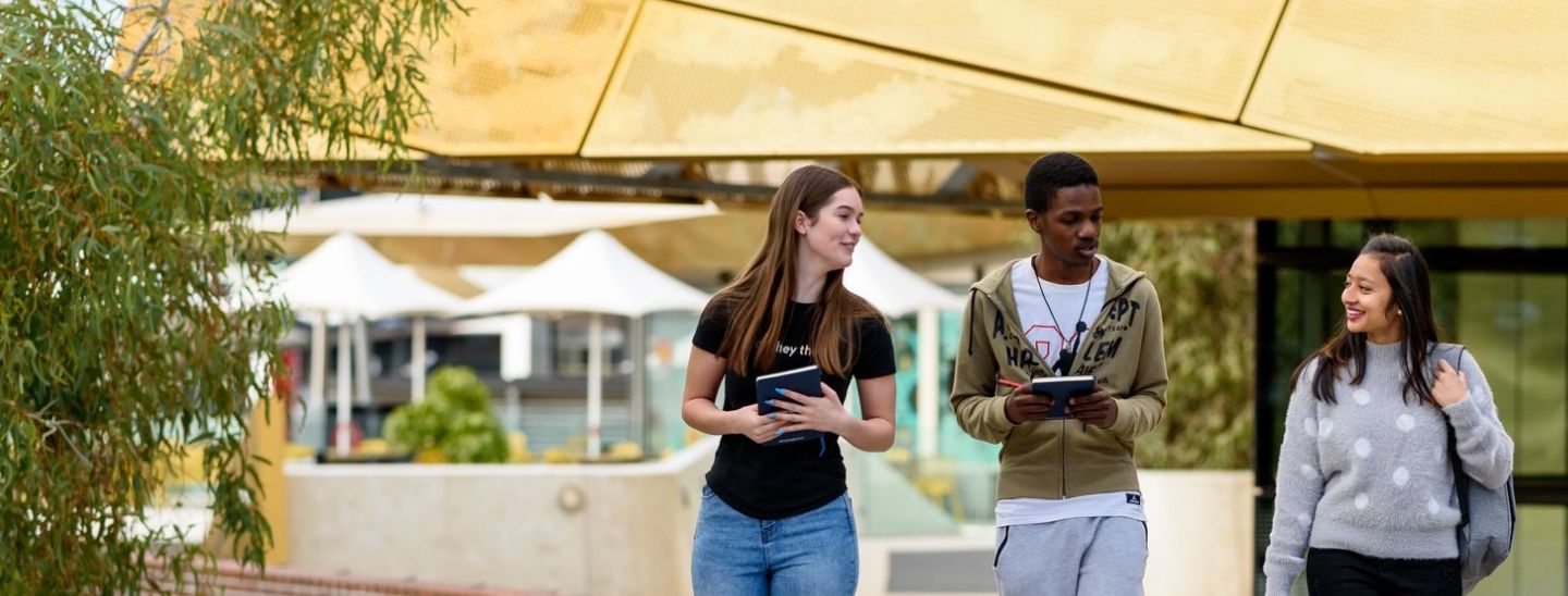 International students walking and talking in campus courtyard with books in hand.