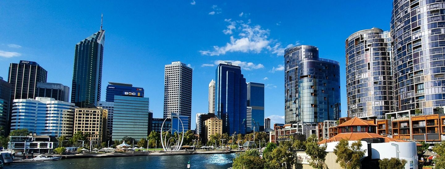 A wide-angle view of the Perth city skyline and Elizabeth Quay under a clear blue sky.