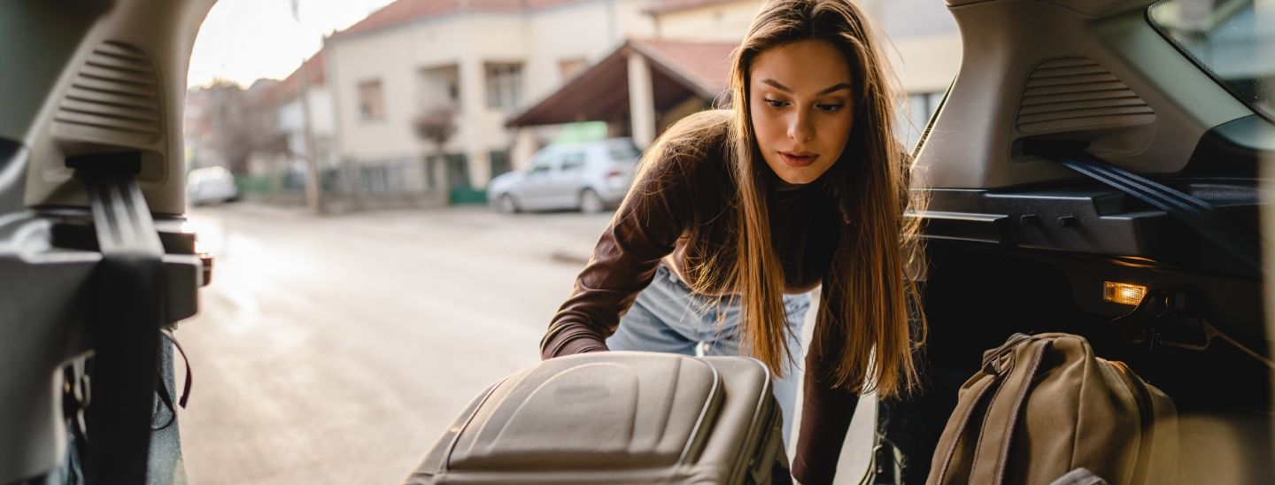 Female student packing suitcase car