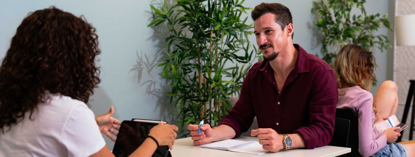 Two person in a supportive face-to-face consultation meeting at a white desk.