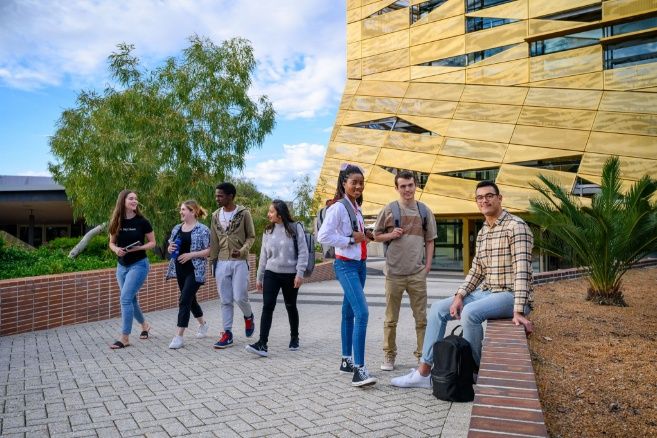 A group of students walking and socialising outside the gold-faceted building at Edith Cowan College.