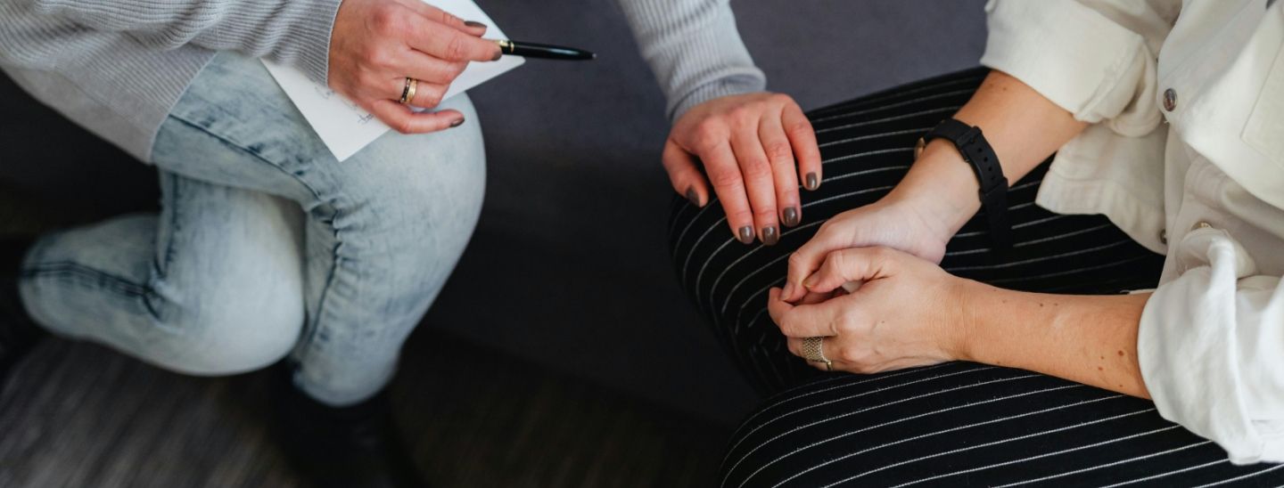 Two people in a supportive counseling session, showing a close-up of hands and a notepad.