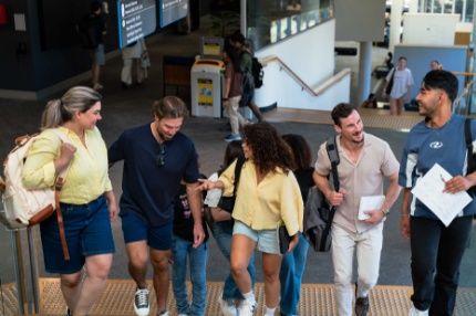 Students carrying backpacks and notebooks, walking together and chatting on a modern indoor campus staircase.