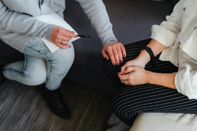 Two people in a supportive counseling session, showing a close-up of hands and a notepad.